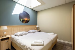 Et hotelværelse med en seng, to sengeborde, en lampe, et ovenlys i loftet og en rund dekoration på væggen.