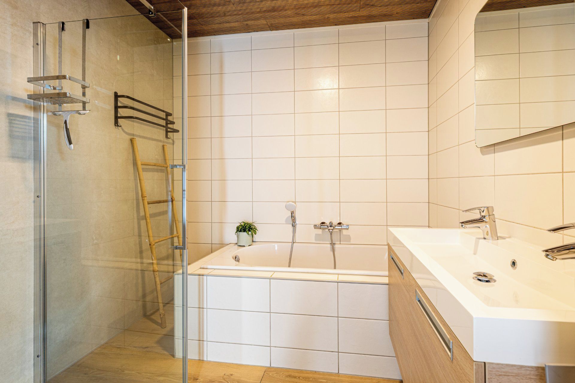 Une salle de bain moderne avec une douche à parois de verre, une échelle en bois, une baignoire et un lavabo blanc avec un miroir.