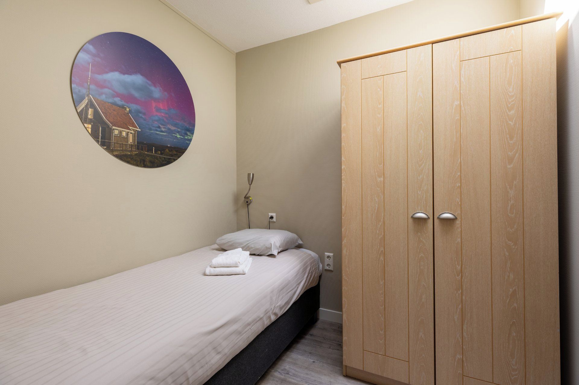 Une chambre avec un lit simple, une armoire en bois et un élément de décoration circulaire fixé au mur.