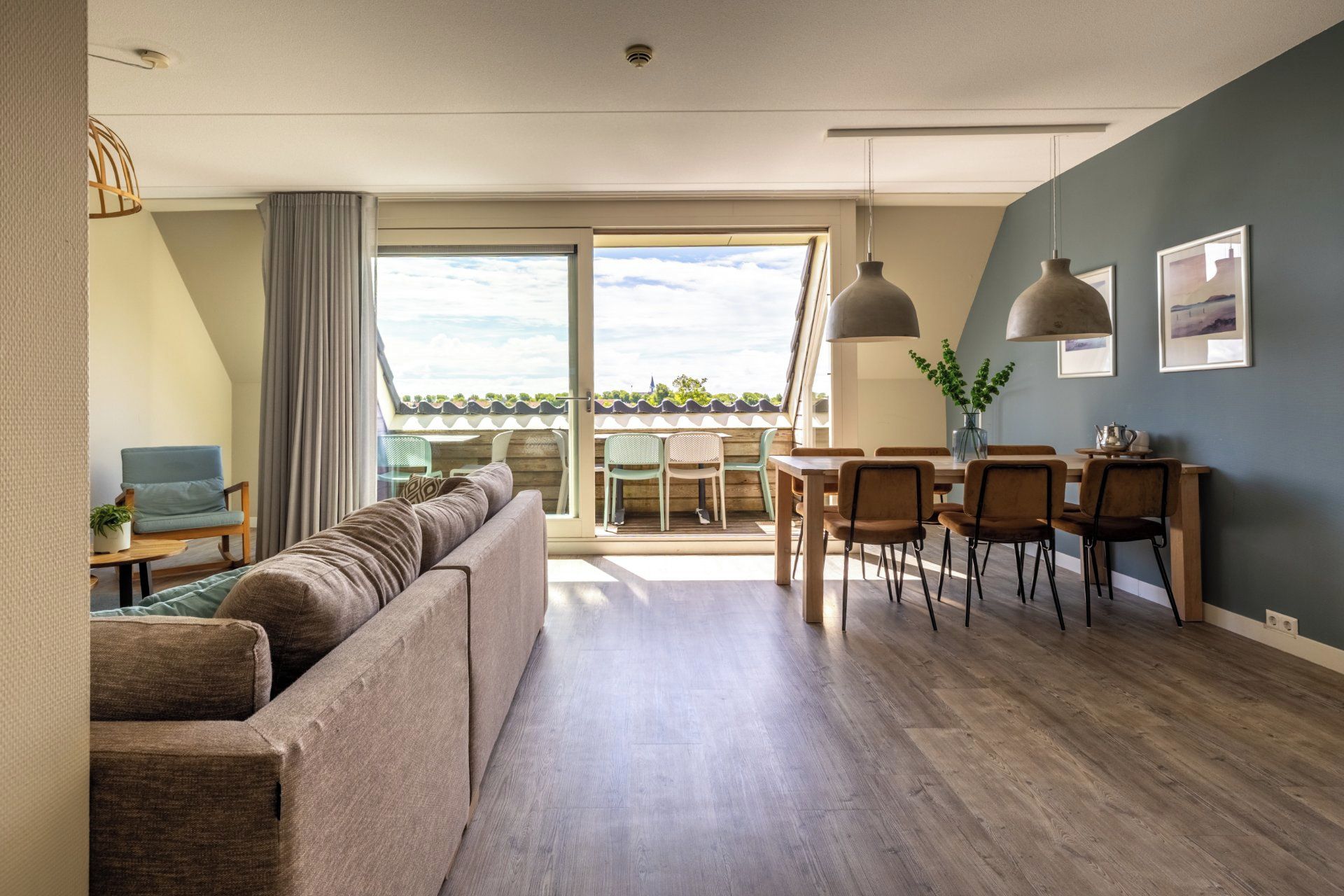 Een moderne woonkamer met een bank, eettafel, stoelen en uitzicht door een groot raam.