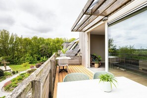 Een balkon met een houten terras, een tafel met stoelen en een bloempot.