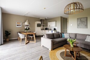 A modern living room with a sofa, dining table, and kitchen in the background. - Enjoy a wonderful stay in this Wellness Apartment with private sauna with 6 people. (Midsland)