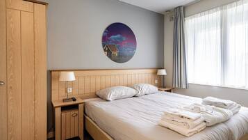 Une chambre d’hôtel comprenant un lit, deux tables de chevet avec des lampes, une armoire et un mur orné d’une œuvre d’art circulaire.