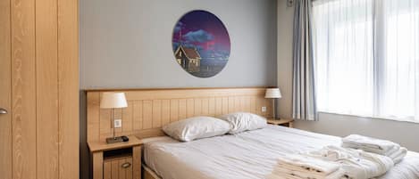 Een hotelkamer met een bed, twee nachtkastjes met lampen, een kledingkast en een muur met een ronde decoratie.