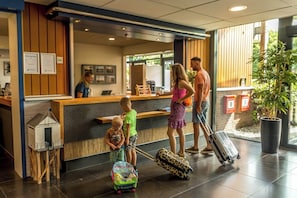 A reception area with a wooden counter, a reception desk, and a large potted plant. - Enjoy a wonderful stay in this Wellness Apartment with private sauna with 6 people. (Midsland)