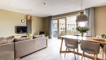 A modern living room with a sofa, TV, and dining area with chairs and a table.