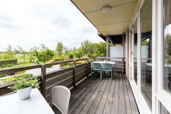 Un espace extérieur abrité, doté d’une table et de chaises, d’une terrasse en bois et offrant une vue sur un paysage verdoyant.