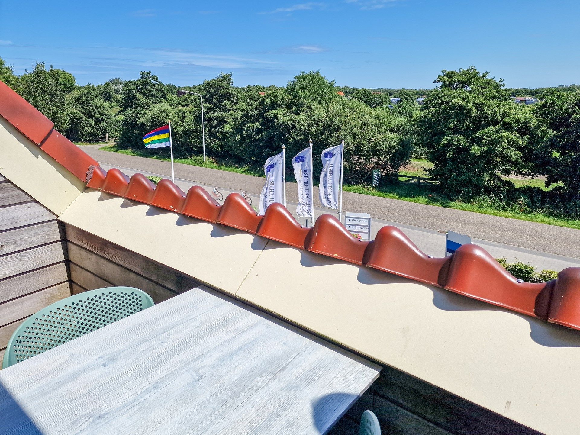 Un balcón con vistas a una carretera y vegetación, con una bandera, banderines y una mesa.
