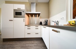 A modern kitchen with white cabinetry, a built-in microwave, a stainless steel range hood, and a coffee maker.