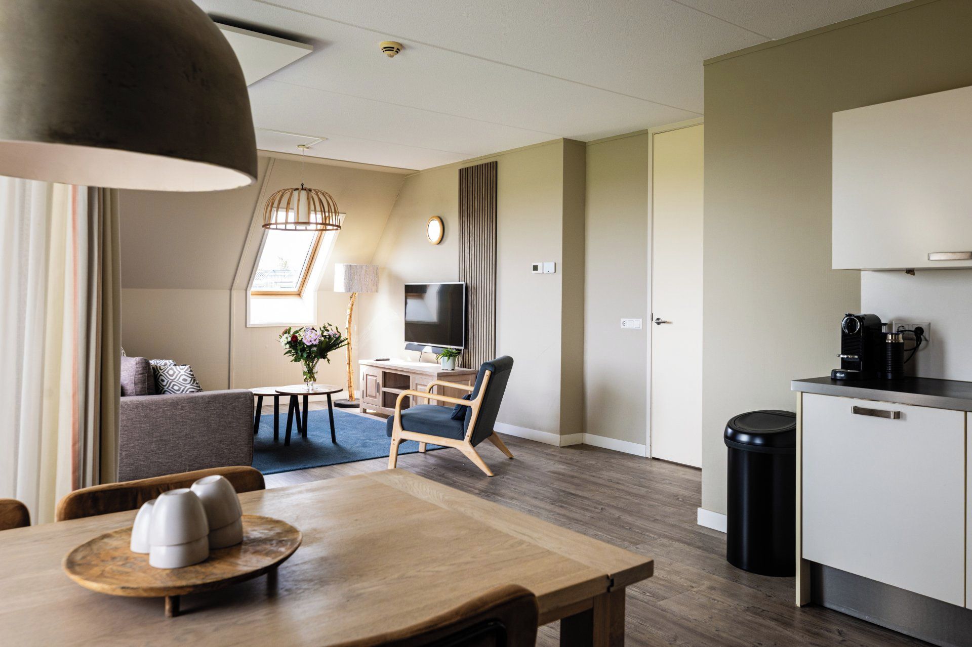 Una habitación de hotel moderna con zona de comedor, sofá, televisor y kitchenette.