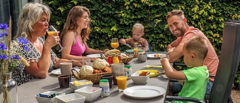 A family dining outdoors with a table set for breakfast, surrounded by greenery.