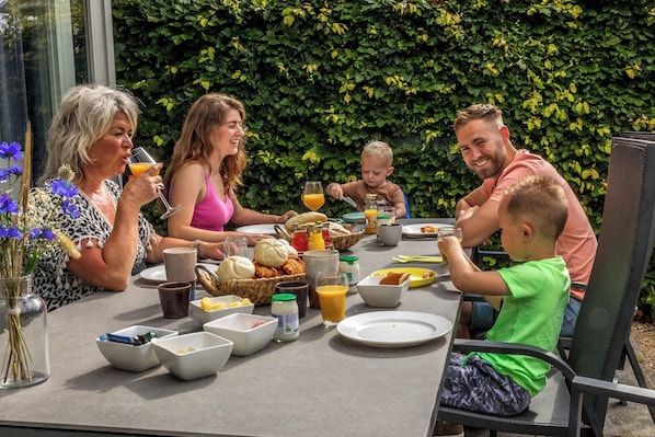 A family dining outdoors with a table set for breakfast, surrounded by greenery.