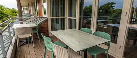 Un patio exterior con cubierta de madera, sillas de metal verde y una mesa.