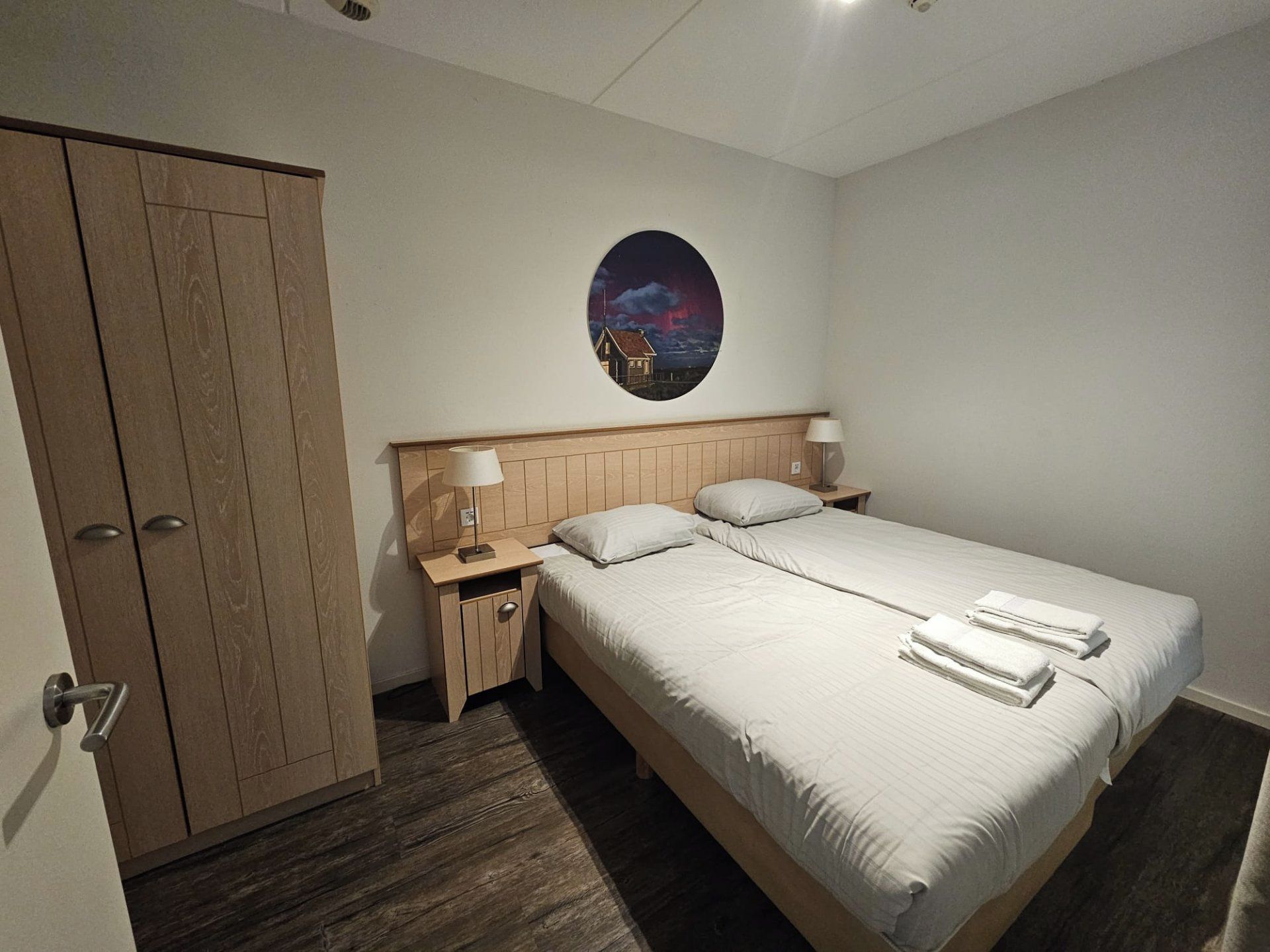 Quarto com cama, mesa de cabeceira, guarda-roupa e um quadro redondo pendurado na parede.