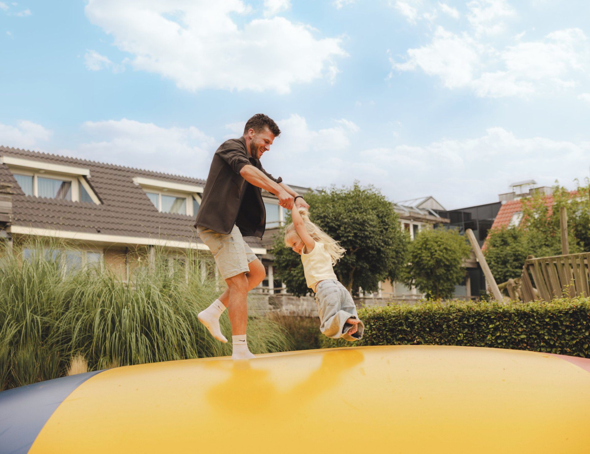 Una persona y un niño sobre una plataforma amarilla inflable al aire libre, con casas al fondo.