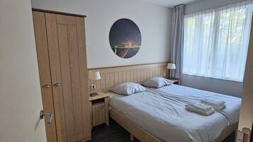 A hotel room with a bed, a nightstand, a wardrobe, a round wall decoration, and a window with curtains.
