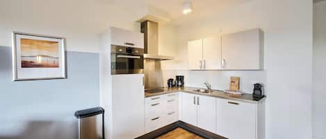 Een kleine keuken met witte kastjes, een roestvrijstalen oven en een koffiezetapparaat.