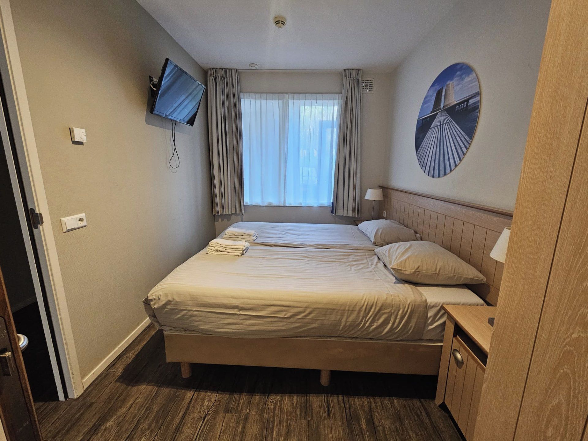 A hotel room with a bed, a television mounted on the wall, and a window with curtains.