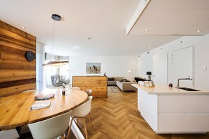 Une cuisine moderne avec une table à manger en bois, des chaises blanches et un îlot central intégré doté d’un évier.