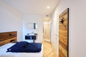 Une chambre moderne avec une tête de lit en bois, une table de chevet, un lit avec une literie aux couleurs sombres, un lavabo intégré et un miroir.
