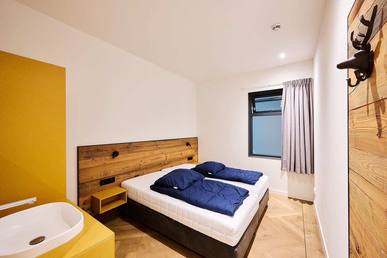 Una camera da letto moderna con una testiera in legno, un'ampia finestra con tende e una vasca da bagno a incasso.