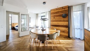 A modern dining area with a round wooden table, white chairs, and a wooden accent wall. - No shortage of luxury in this exclusive and very spacious apartment. There are five bedrooms, each with its own shower. Enjoy the tranquility and space... (Midsland)