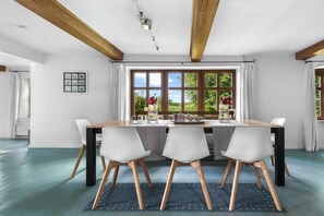 A dining area with a table set for four, wooden beams on the ceiling, and a view of greenery outside. - Holiday apartment with 1 bedroom (Steinberg)