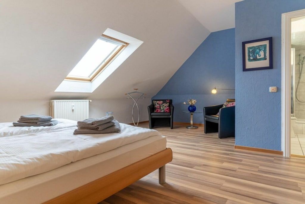 Une chambre avec un puits de lumière, un lit, une chaise, une petite table avec un vase et un espace douche.