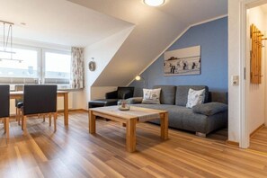 A modern living room with a sofa, a coffee table, and a dining area with chairs and a table. - Utholm 10 - Black-headed Gull (St. Peter-Ording)