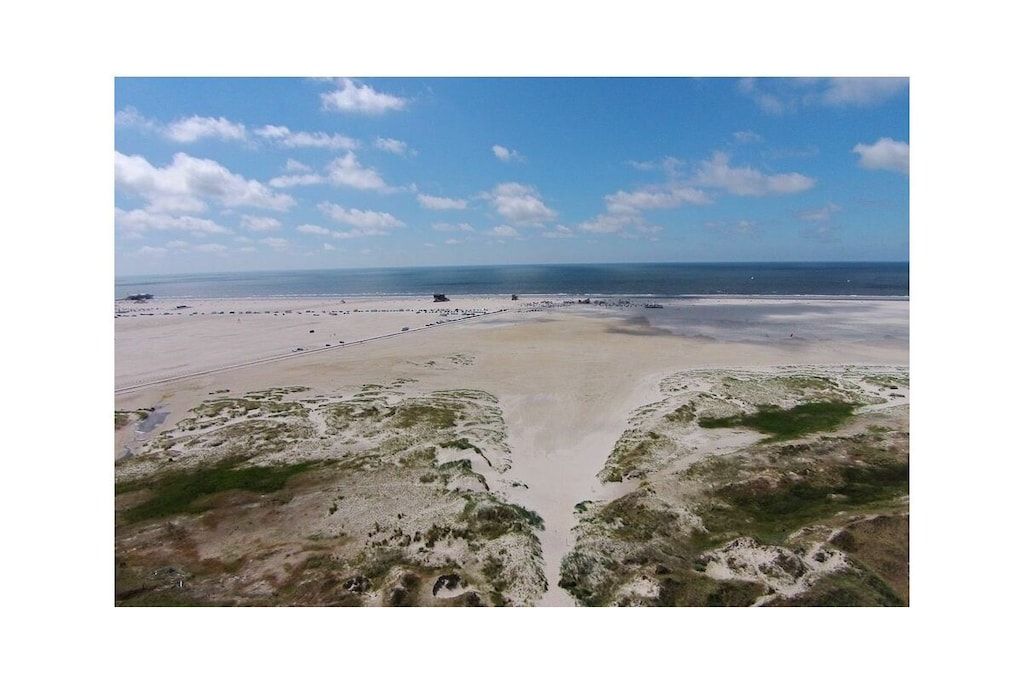 Ein Strand mit blauem Himmel, sandigem Gelände und vereinzelten Gebäuden.