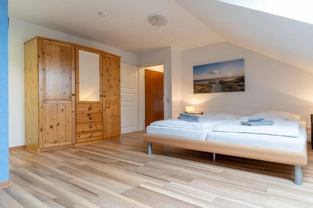 Ein Schlafzimmer mit einem großen Holzschrank, einem Bett mit weißer Matratze und einem Landschaftsbild an der Wand.