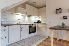 A kitchen with white cabinets, a stainless steel sink, and a wooden table with a vase. - Utholm 10 - Black-headed Gull (St. Peter-Ording)