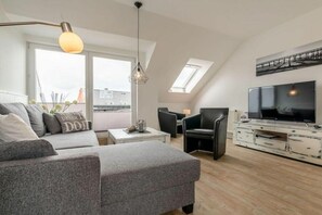 Ein modernes Wohnzimmer mit einem grauen Sofa, schwarzen Sesseln, einem Fernseher und einem weißen Schrank.