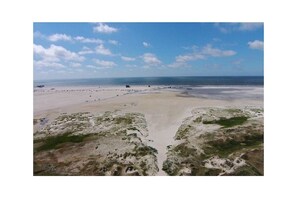 A beach with a clear sky, sandy terrain, and a few scattered structures. - Utholmer 16 - Lighthouse (St. Peter-Ording)