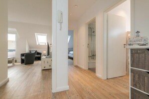 A spacious room with a wooden floor, a bed, a desk with a chair, and a small table with a lamp. - Utholmer 16 - Lighthouse (St. Peter-Ording)
