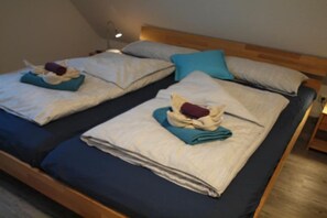 Two twin beds with folded towels and pillows, a wooden headboard, and a bedside table with a lamp. - Holiday home in Wittmund with swimming pool (Wittmund)
