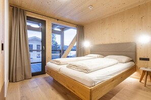 A wooden-paneled room with a bed, a window, and a door. - Superior Chalet # 26 with Sauna & Hot Tub (Turrach)