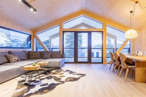 A modern interior with a wooden ceiling, a large window, a sofa, a dining area, and a cowhide rug.