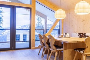 A wooden dining area with a large table and chairs, large windows, and a view of a building outside. - Superior Chalet # 26 with Sauna & Hot Tub (Turrach)