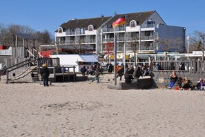 Un bâtiment situé au bord de la plage, doté de nombreux balcons, avec un premier plan sablonneux et un ciel dégagé.