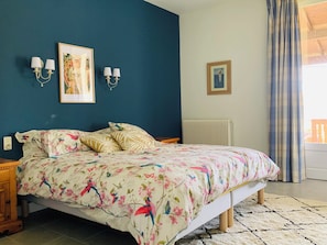 A bedroom with a bed, two wall-mounted lamps, a framed picture, a radiator, and a window with curtains.