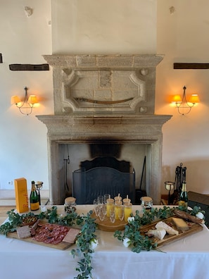 A fireplace with a stone mantle, flanked by wall-mounted lamps, and a table set with a charcuterie board, glasses, and bottles.