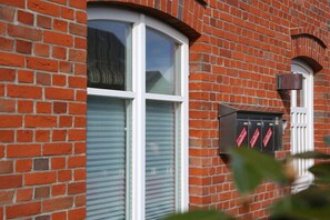 A brick building with a large window and a mailbox. - Different Living Holiday Apartment 06 Flood (Westerland)