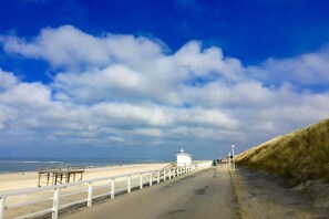 A beach with a white fence, a small white building, and a grassy dune. - Different Living Holiday Apartment 06 Flood (Westerland)