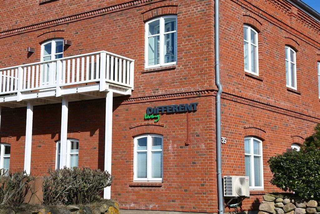 Un bâtiment en briques rouges doté d’un balcon, d’une enseigne indiquant « DIFFERENT living » et du numéro « 35 » sur la façade.