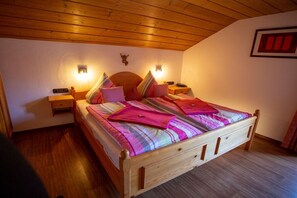 A wooden bed with a colorful blanket, two bedside tables with lamps, and a wall-mounted light fixture. - Holiday apartment with 2 bedrooms (Ruhpolding)