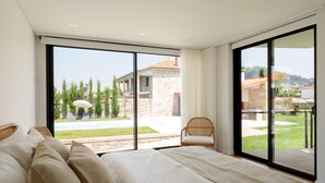 Een slaapkamer met een groot bed, een stoel en uitzicht op een zwembad en gebouwen.