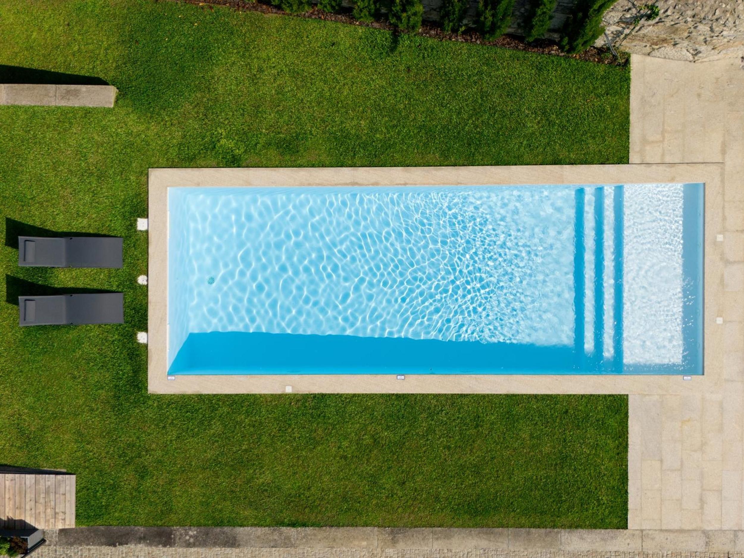 Una piscina rectangular con agua cristalina, rodeada por un césped cuidado y dos sillas de descanso.