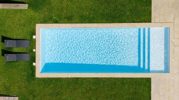 Una piscina rectangular con agua cristalina, rodeada por un césped cuidado y dos sillas de descanso.