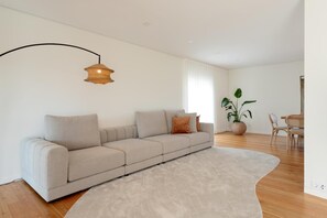 Una sala de estar moderna con un sofá color beige, un tapete redondo, un comedor con mesa y sillas, y una planta en maceta.